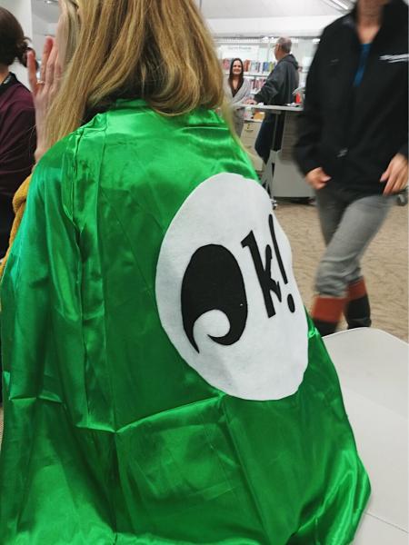 Photo of a Toi Ohomai staff member wearing a bright green cape with a large koha logo on it