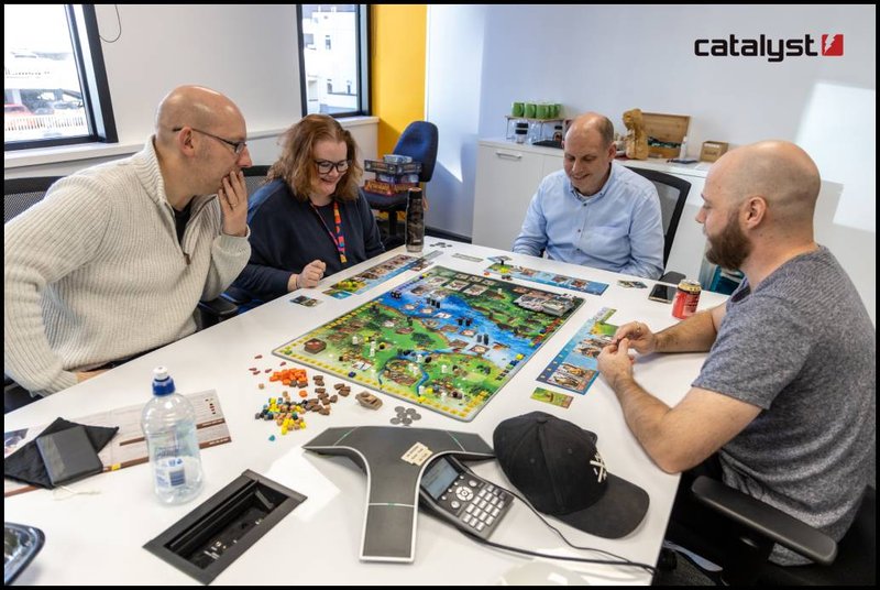 Four people sittting at a table playing a board game.