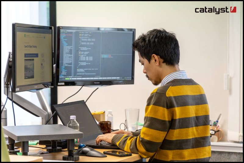 Looking over a person&#x27;s shoulder at coding on a few computer screens.