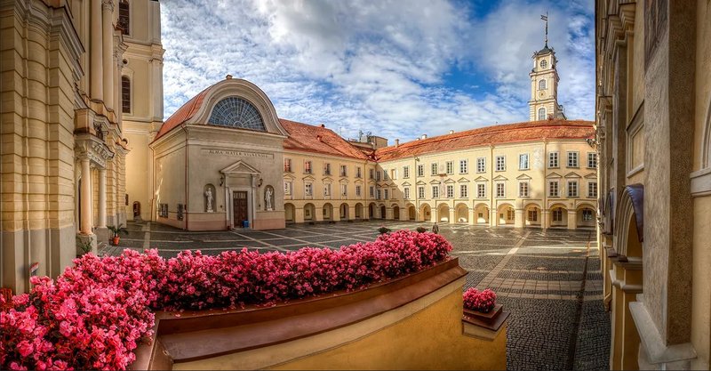 Outside view of the historic Vilnius University with pink flowers in the foreground and a blue sky with clouds